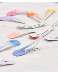 Close-up of colorful glitter teardrop metal snap hair clips on beige linen fabric