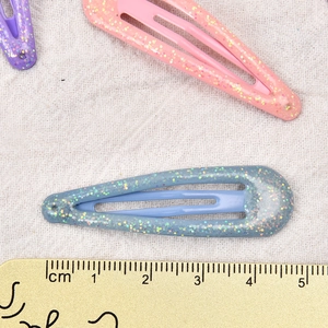 Set mit 5 cm bunten Glitzer-Haarspangen in Tropfenform für Mädchen auf weißem Stoffhintergrund