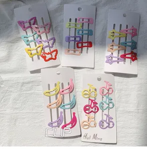 Détail de barrettes colorées en formes de papillon, étoile et fruits sur une carte blanche