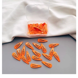 Leuchtend orangefarbene Haarclips in einer transparenten Box auf weißem Stoffhintergrund