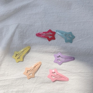 Détail de six barrettes étoiles en métal coloré disposées sur une surface en lin blanc