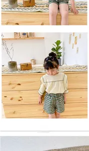 Girl's summer set with beige puff sleeve top and green checkered shorts in a cozy interior