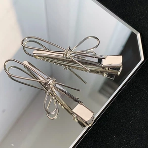 Detail of silver metallic bow hair clips with a polished mirror finish on a reflective base