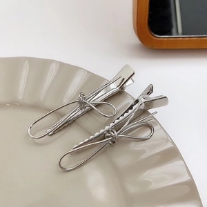 Detailed view of two silver metal bow hair clips on a white ceramic plate