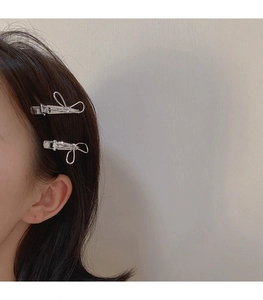 Close-up of two silver minimalist wire bow hairpins styled on a model's side hair