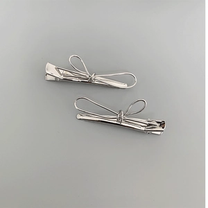 Detailed view of two polished silver metal bow hair clips on a smooth gray surface