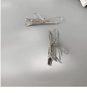 Detailed view of two minimalist silver metal bow hair clips with elegant duckbill design
