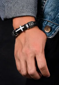 Detail of men's woven leather bracelet featuring silver cross and knurled metal elements