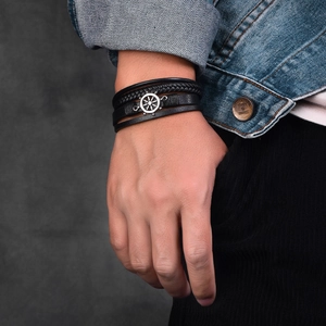 Detailaufnahme eines geflochtenen Lederarmbands mit silbernem Steuerrad für Herren