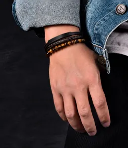 Detail of men's multilayer tiger eye bead and woven leather bracelet set worn on wrist