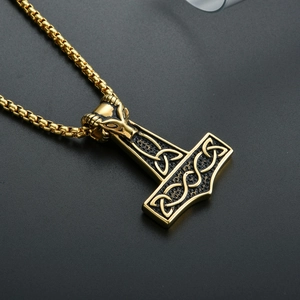 Detail view of golden Mjolnir pendant with goat head design and Celtic knot patterns