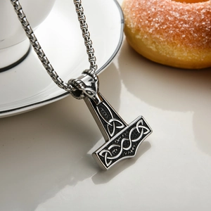 Macro shot of silver Thor's Hammer pendant with ram head and Celtic knot on light surface