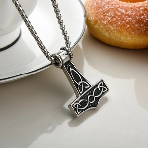 Detail of silver stainless steel Mjolnir pendant with Nordic knots on white background