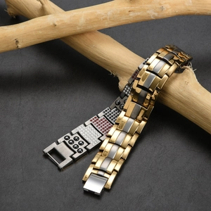 Detalle de pulsera de magnetoterapia de titanio con eslabones oro y gris sobre ramas