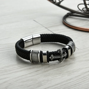 Détail du bracelet en cuir tressé noir avec croix argentée sur une table en bois