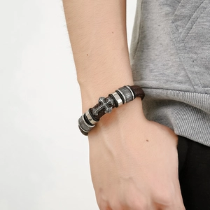 Gros plan d'un bracelet en cuir tressé marron vintage avec croix argentée et fermoir aimanté
