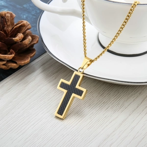 Herren Kreuzkette aus goldenem Titan mit schwarzer Kohlefaser-Einlage auf einer weißen Tasse