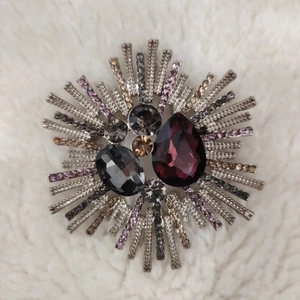Macro view of crystal brooch with purple teardrop gemstone on white faux fur background