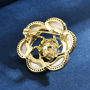 Broche camélia dorée en nacre avec perle et fermoir à épingle sur tissu bleu foncé