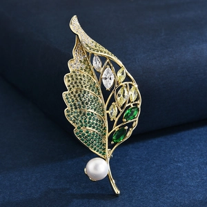 Élégante broche feuille dorée avec zircons verts et perle blanche sur fond bleu foncé