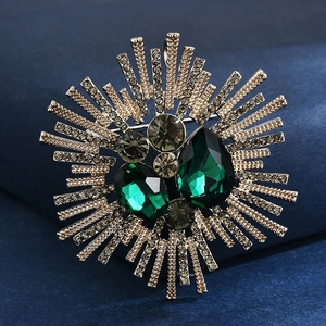 Detailed close-up of emerald green crystal brooch with vintage gold sunburst design