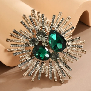 Detailed macro view of crystal sunburst brooch with emerald green stones and silver finish