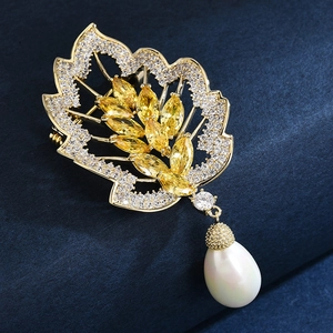 Elegant gold leaf pearl brooch with sparkling crystals on dark blue fabric background