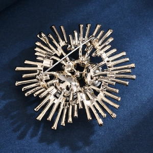 Back view of a gold-plated sunburst brooch with green gemstone on blue fabric