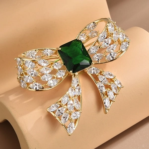 Bow brooch with emerald green stone and sparkling zircons in a luxury golden setting