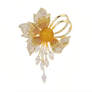 Elegant gold-plated flower brooch with amber stone and dangling zircon tassels on white background