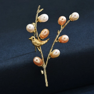 Elegant golden bird on branch brooch with colorful freshwater pearls on blue surface