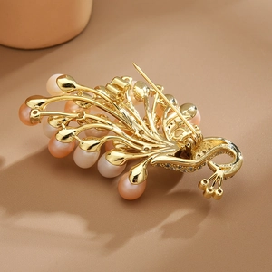 Elegant gold phoenix feather brooch with freshwater pearls on a warm brown background