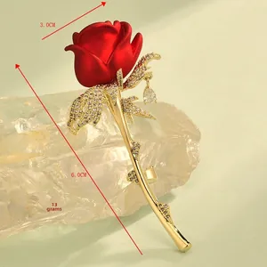 Détail d'une broche rose en émail rouge avec feuilles d'or et cristaux blancs