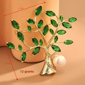 Detail view of a gold tree brooch with green marquise gems and a large white pearl