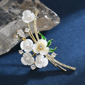 Broche fleurie élégante en or avec pétales de nacre et feuilles vertes sur fond bleu
