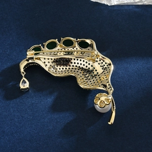 Elegant gold leaf brooch with green zircon and pearl drop on blue velvet background