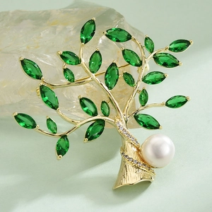 Elegant gold tree brooch with green gemstone leaves and white pearl accent on stone