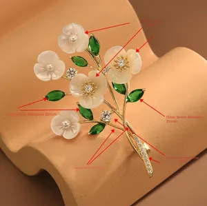 Detailed macro view of white shell flower brooch with sparkling green zirconia leaves