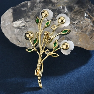 Elegant gold flower brooch with white petals and green stones shown from back view