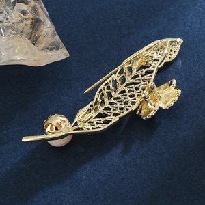 Elegant gold feather brooch with a white pearl on a deep blue velvet background