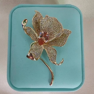 Macro detail of orchid brooch with gold setting, white zircon petals and orange gemstone
