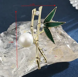 Dettaglio macro di una spilla in bambù dorato di 4,5cm con foglie in smalto e perla bianca