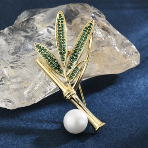 Broche bambou élégante avec cristaux verts et perle blanche sur fond bleu texturé