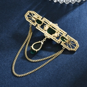 Vintage-Brosche in Gold mit Smaragdsteinen und eleganten Quasten auf dunklem Blau