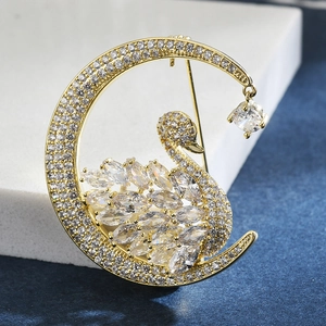Macro shot of gold moon and swan brooch with micro-paved zircons and hanging crystal pendant