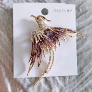 Macro detail of phoenix brooch with purple enamel wings and sparkling crystal inlay
