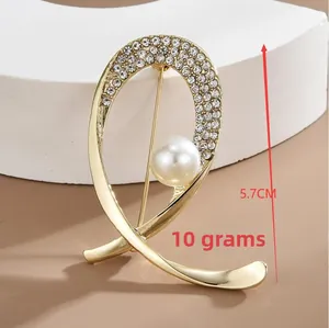 Detail of a 5.7cm gold brooch with rhinestones and a white pearl on a display stand