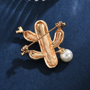 Broche cactus dorée avec perle et métal texturé sur fond en velours bleu profond
