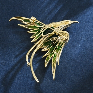Elegant gold-plated phoenix bird brooch with emerald green enamel on dark blue velvet
