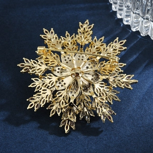 Elegant gold snowflake brooch with pearls and rhinestones on a dark velvet background